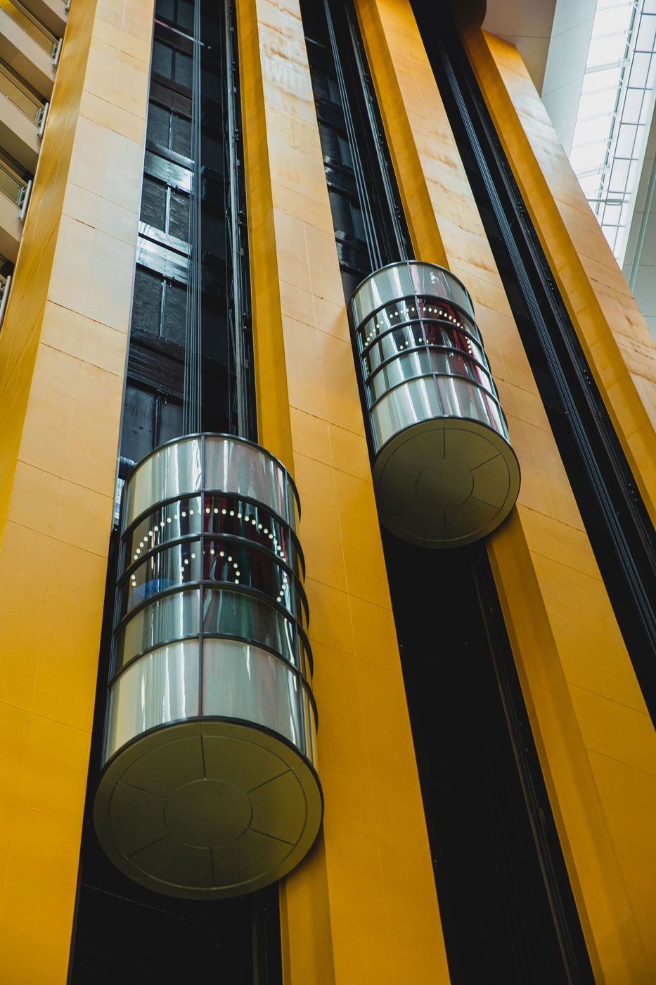Glass capsule lifts running up a building with yellow walls