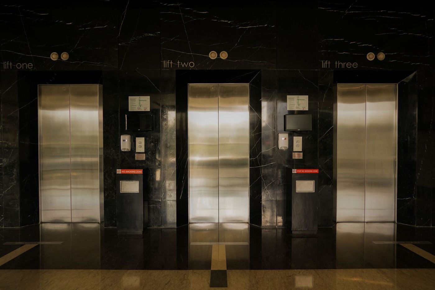 Row of three stainless-steel lifts in a dark lobby